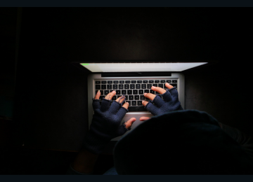 A hacker with half-finger gloves at a laptop, indicative of a cyberattack.