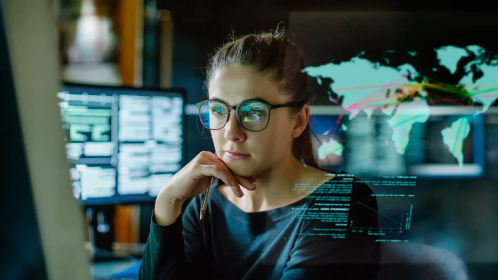 Data analyst wearing glasses working at computer with code displays